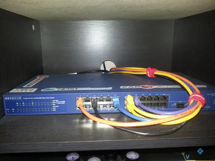 Netgear GS724Tv3 switch on a shelf with color-coded network cables