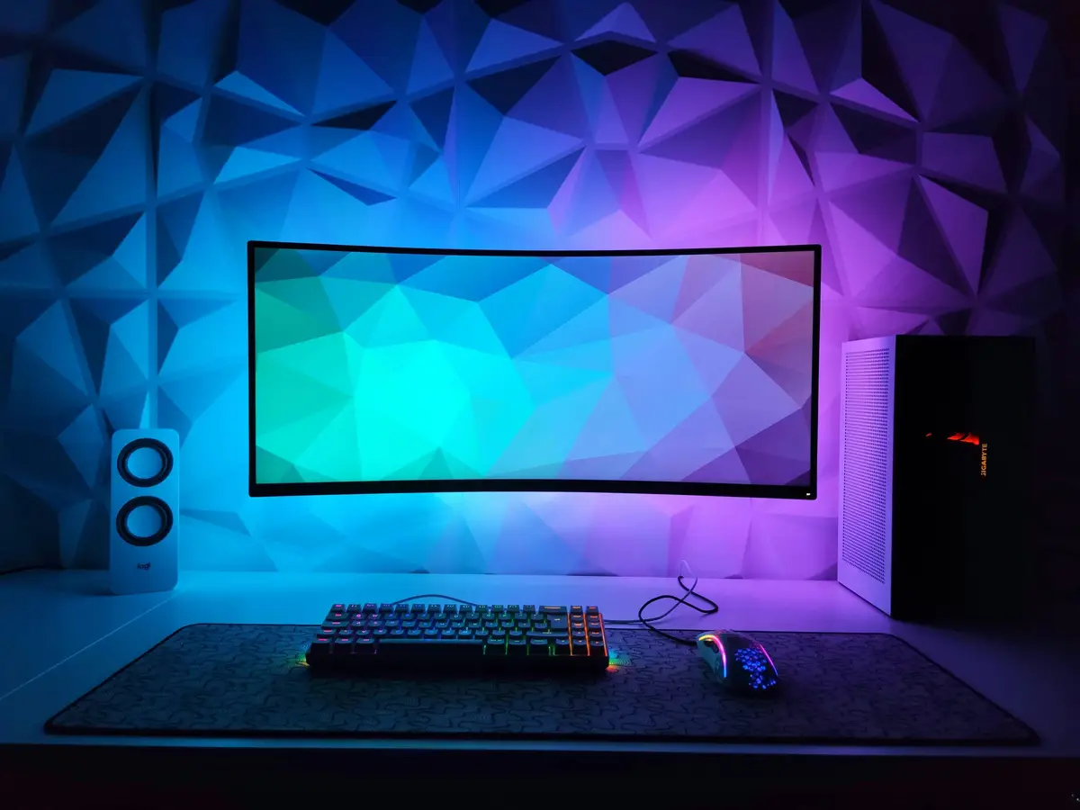 Gaming monitor and keyboard against a wall with blue and purple lighting