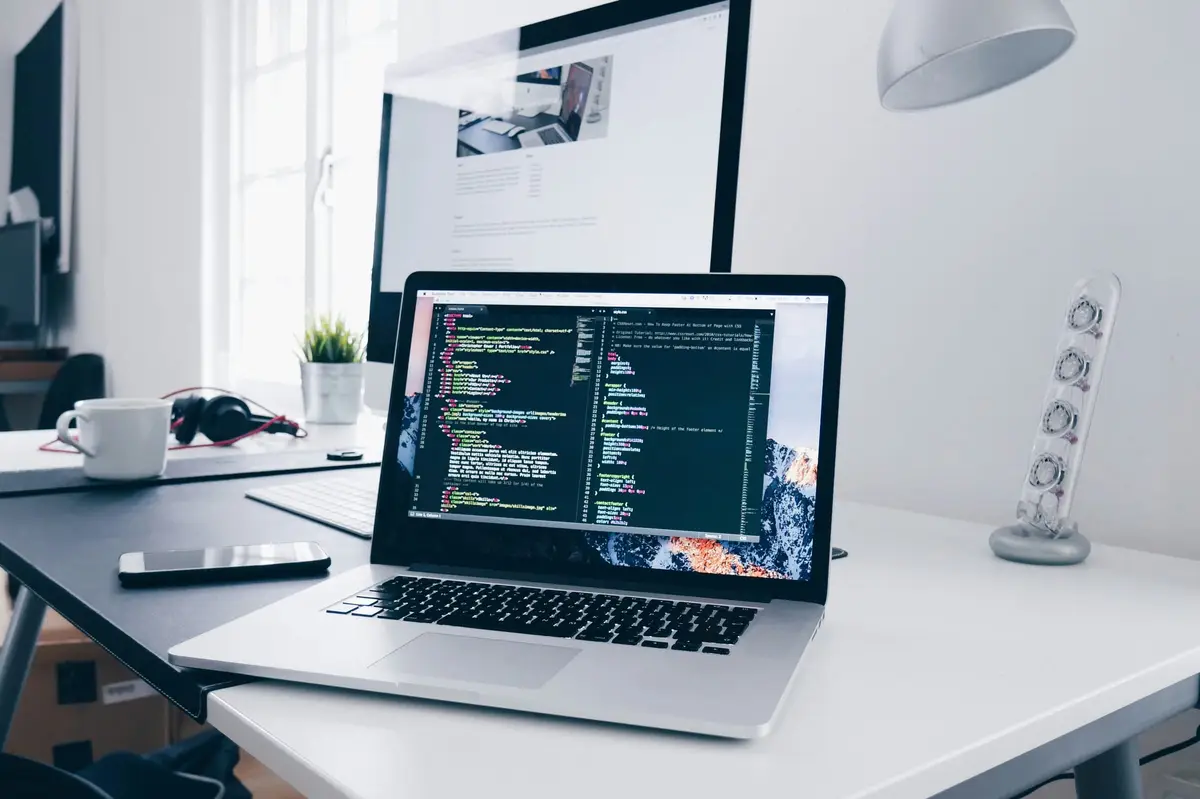 Laptop displaying code on a bright desk with an external monitor