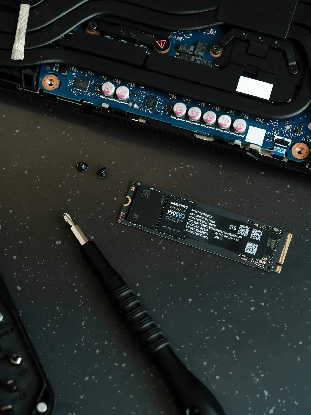 M.2 solid-state drive beside an open laptop and a screwdriver