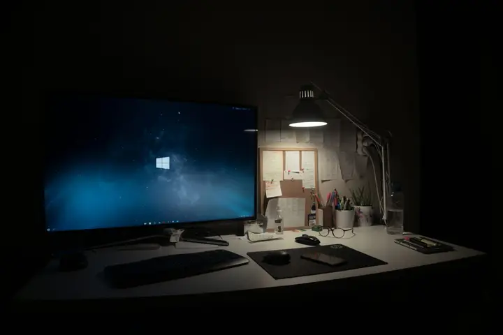 Desktop monitor showing Windows beside a desk lamp and keyboard